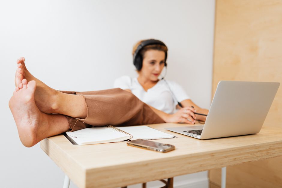 Woman working remotely while relaxing with feet up at home office desk using laptop.
