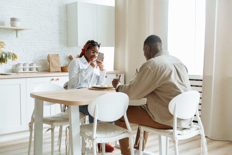 African couple enjoying breakfast while capturing moments on phone at a cozy dining table.