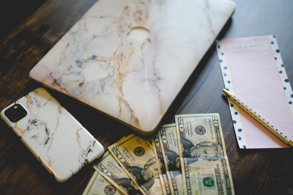 Stylish workspace with marble tech accessories, US currency, and a notepad on a wooden desk.