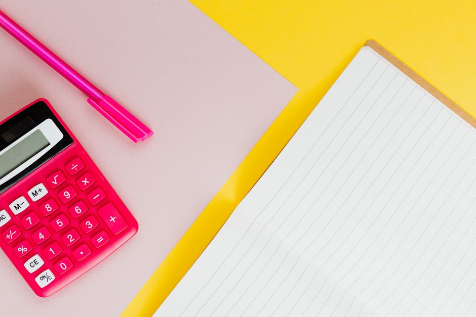 Vibrant pink calculator and pen on a colorful background with a lined notebook for office or school use.
