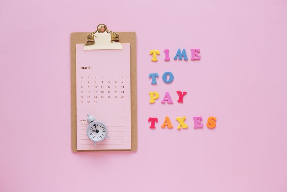 A flat lay of a March calendar and 'Time to Pay Taxes' letters on a pink background.