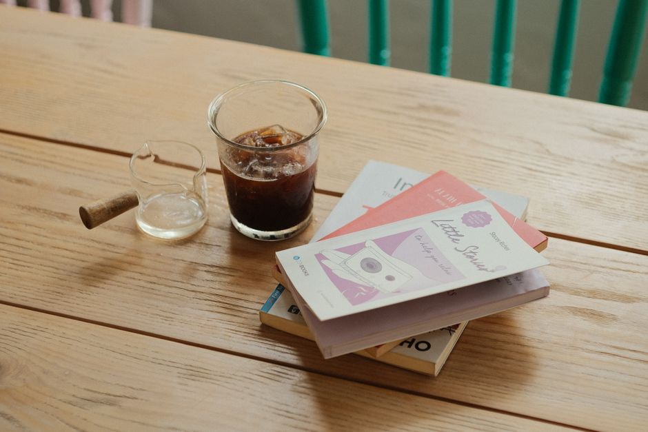 A glass of iced coffee and books on a wooden table, creating a cozy reading atmosphere.