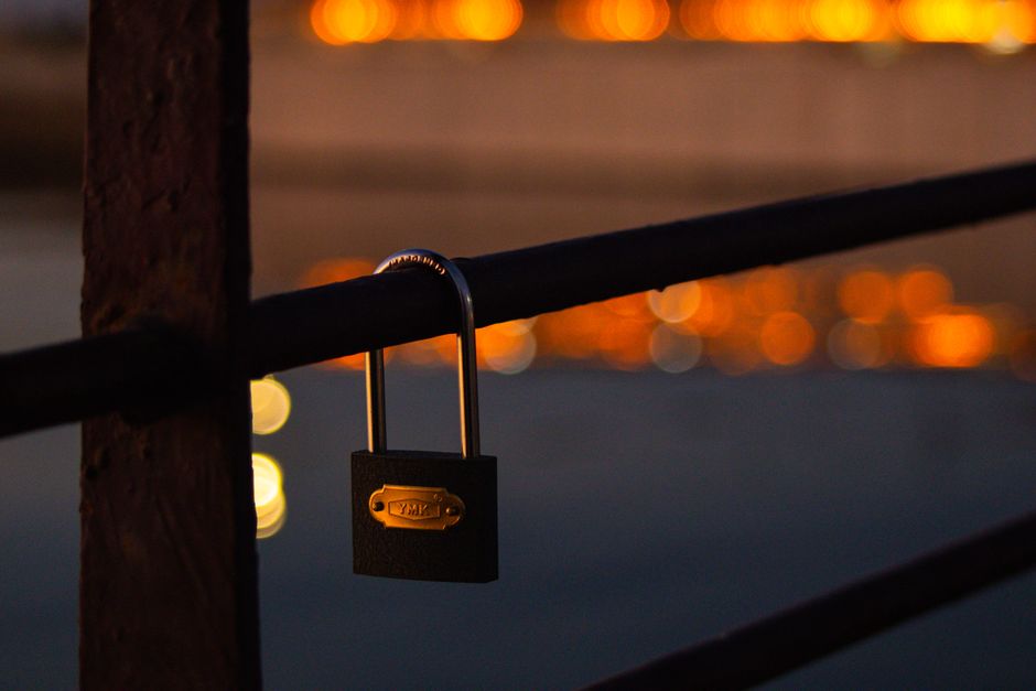 A close-up of a locked padlock on a fence with bokeh lights at twilight.