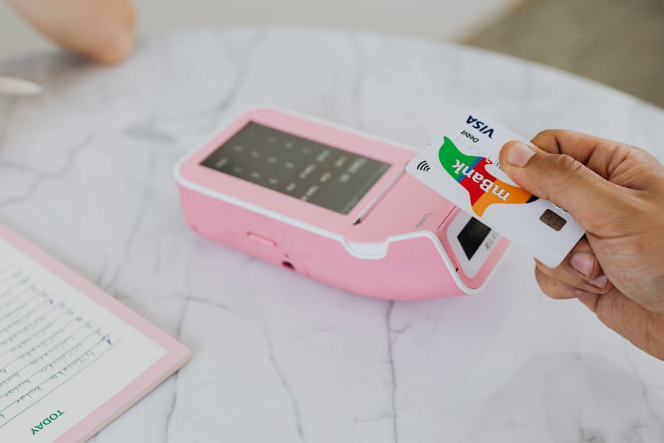 A hand using a Visa card for a contactless payment on a pink terminal.