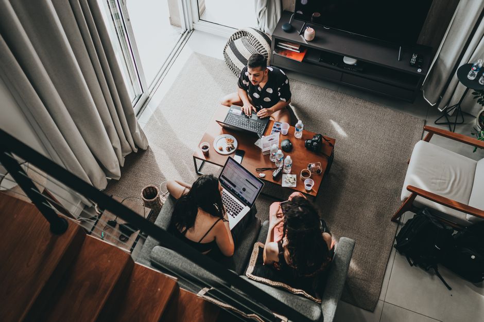 From above of young male and female remote workers sitting together around table with drinks and working on laptops