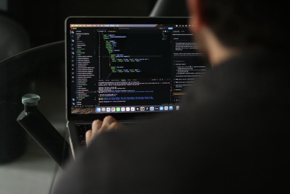A focused developer writing code on a laptop in an indoor workspace.