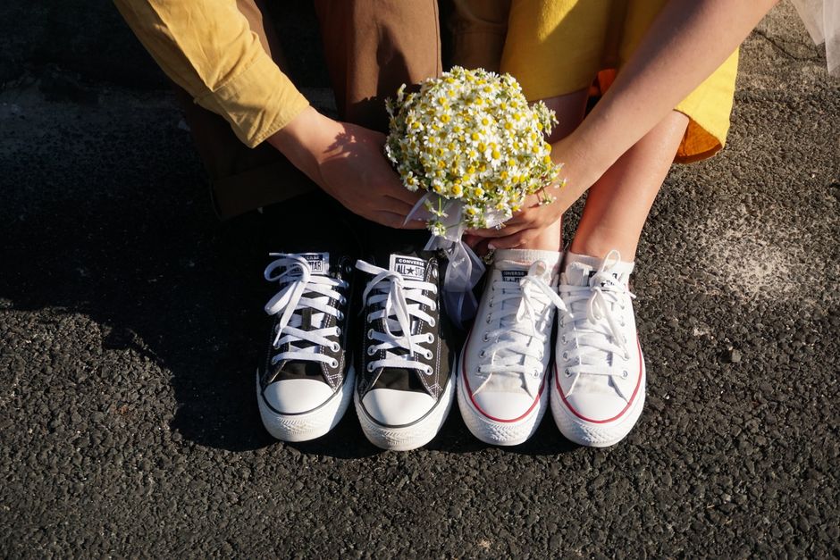A couple sitting on asphalt with daisy bouquet and sneakers on a sunny day.